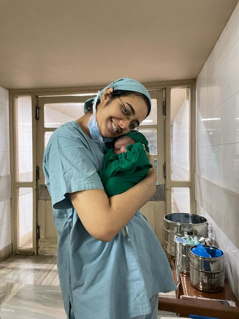 Dr. Sejal Kulkarni in clinical scrubs holding a newborn baby